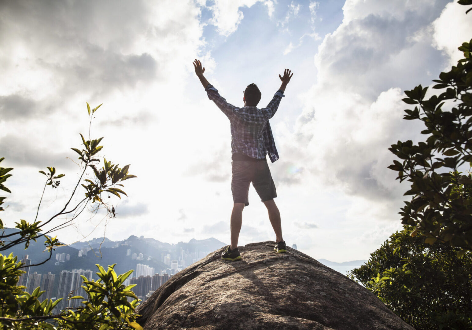Man standing with arms up from rock formation in nature, Hong Kong, China, from Braemar Hill Peak